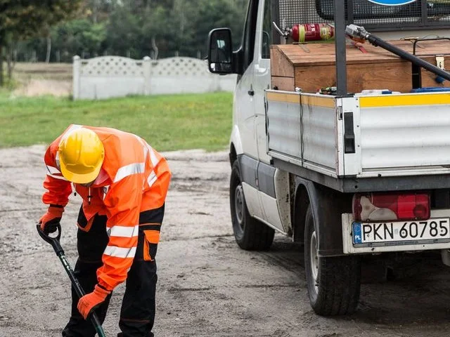 Közútüzemeltetési szakember kátyút javít az útpadka mellett álló szervizautó mellett